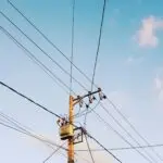 Low-angle shot of electricity poles and wires against a clear blue sky.